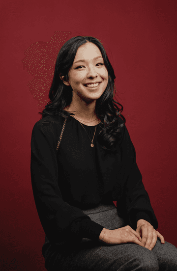 A portrait of Naomi Suzuki in front of a red backdrop.