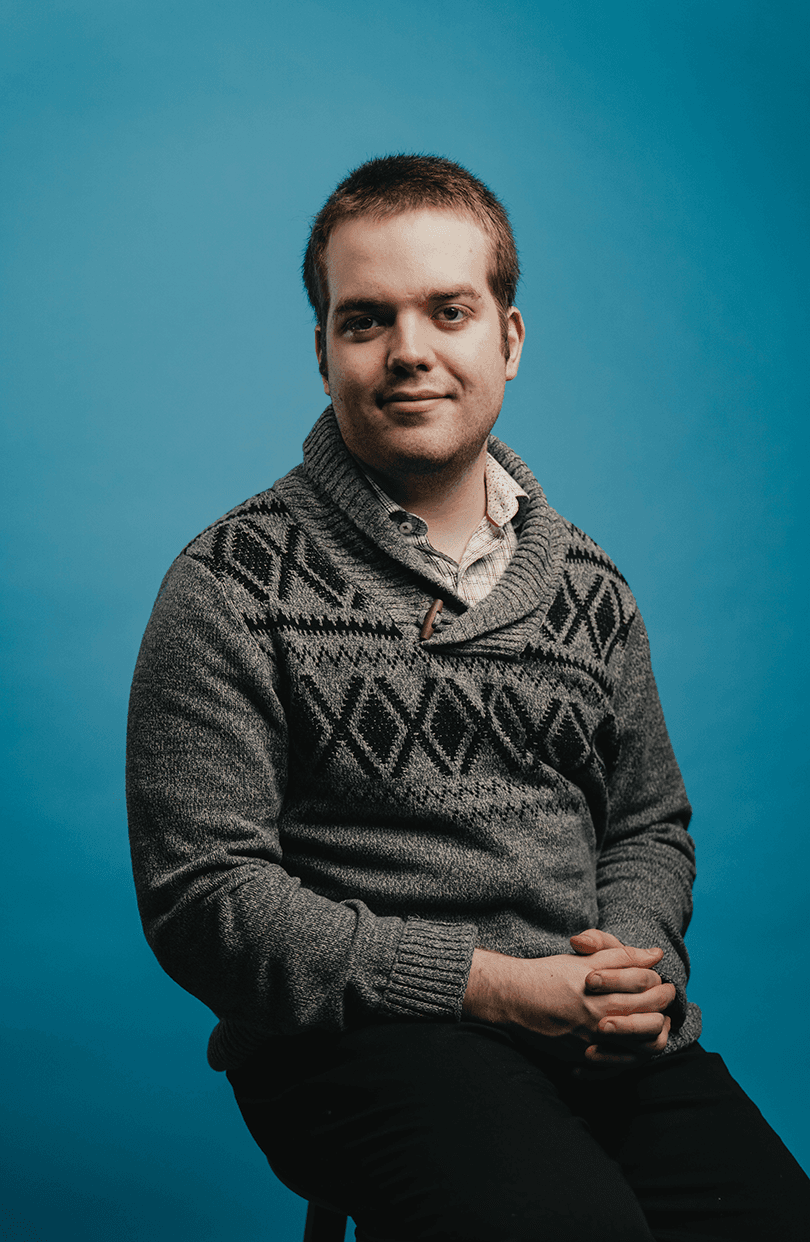 A portrait of Spencer Arshinoff in front of a blue backdrop. Image 1 of 3